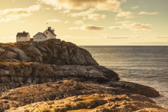 A lighthouse and house on rocky cliffs by the ocean at sunset, creating a serene coastal scene,