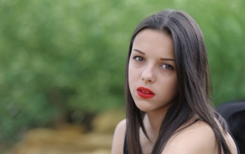 Young beautiful serious brunette girl with red lips and long straight hair over green nature
