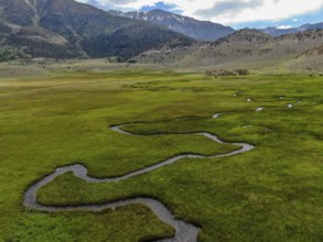 Aerial view of green land and small curve river with mountain in the background in Aspen Springs,