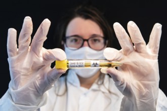 Selective focus shot of vial filled with urine sample and labeled Covid-19 test, held center frame