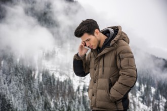 Dark haired handsome young man in winter outerwear using cell phone or smartphone, outdoor at