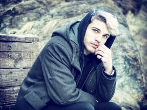 Portrait of young man in hoodie posing outdoor in winter setting with snow all around, looking at