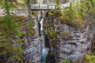 Tourist bridge over a magnificent cascading waterfall in a picturesque gorge Maligne Canyon. Cool