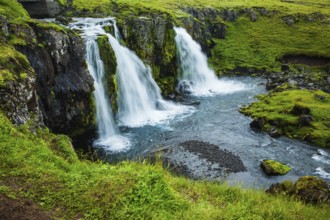 Cascading waterfall Kirkjoufellfoss at the foot of the mountain Kirkjoufell. Summer in Iceland.