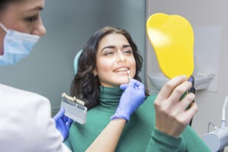 Female dentist, patient holding mirror. Tooth shade chart