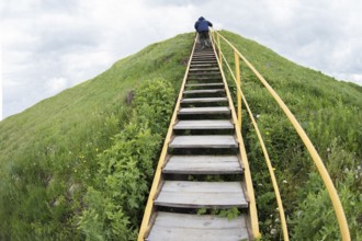 A man climbs up a hill on a ladder