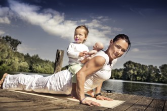 Young woman and her little daughter making yoga exercise at a lake