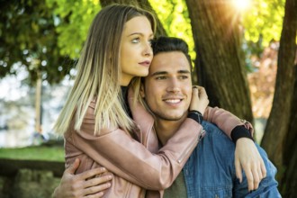 Boyfriend and girlfriend standing in countryside in green luscious field, embracing each other and