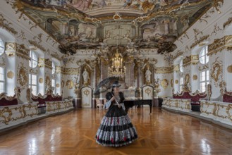 A woman in a black dress stands in a magnificent room with frescoed ceilings, staged photo shoot,