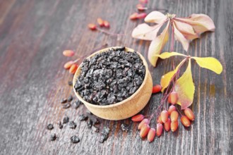 Dried black barberry in a bowl, sprigs with fresh berries and leaves on dark brown wooden board