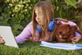 Blond kid girl selfie photo with tablet pc and dog lying on grass