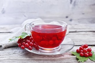 Tea with viburnum in a glass cup, berries and green leaves, burlap on wooden board background
