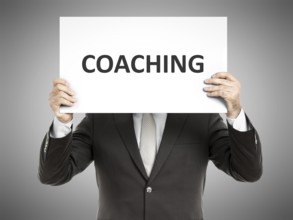 A business man holding a paper in front of his face with the message coaching