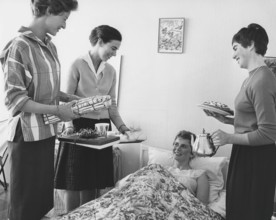 Birthday in the 1960s. A young woman lies in bed and is surprised by her girl friends singing happy