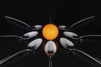 Teaspoons and orange golf ball on the black glass table