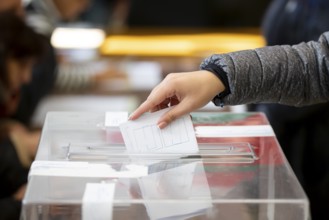 A woman casts her envelope vote into a transparent plastic ballot box. Human hand voting