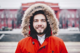 Portrait, close-up of young stylishly man smiling with a beard dressed in red winter jacket with a