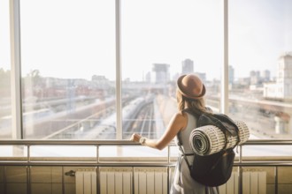 Traveler Rear view woman standing at the window in hall Train Station departure with backpack,