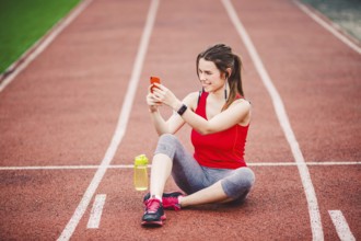 Beautiful fitneß girl uses smartphone at stadium after workout. Sports and healthy. Sport woman use