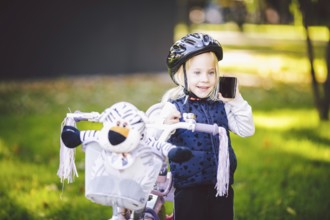 Funny child Caucasian girl blonde in a bicycle helmet near a purple bike with a basket in outside