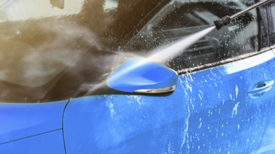 Side mirror of blue car washed in self serve carwash, jet water sprays from high pressure nozzle,