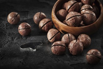 Macadamia Nuts And Key For Open It With Wooden Bowl On Black Background