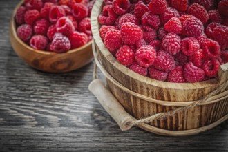 Bowl and bucket with raspberries on wooden board