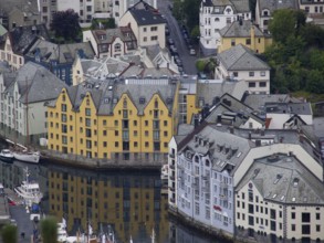 Yellow and white houses are reflected in the canal, surrounded by several small boats, alesund,