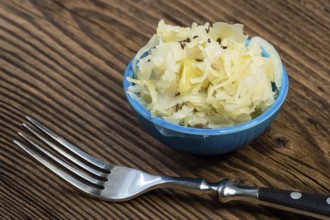 Homemade pickled sauerkraut in a bowl with a fork on a wooden board