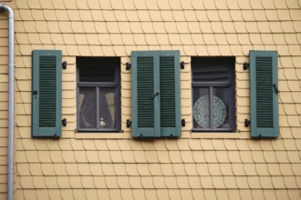 Open shutters on a striking façade of yellow shingles