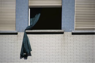 A loose curtain blows out of the window of a brick-built residential building