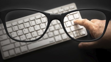 Some black glasses with keyboard sharp and blurred