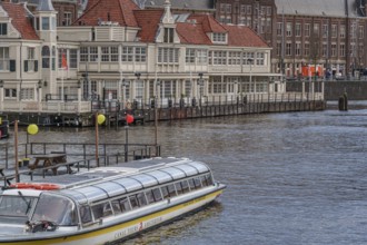 Houseboat in front of a historic building with red roofs on the canal, Amsterdam, Netherlands