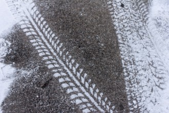 Tyre tracks on snow-covered asphalt, high-contrast texture in winter