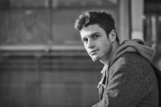 Handsome young man in city setting, lit by sunset light, looking at camera in a black and white