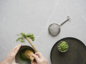 Preparation of green tea drink with matcha powder. Hands with traditional bamboo whisk over bowl of