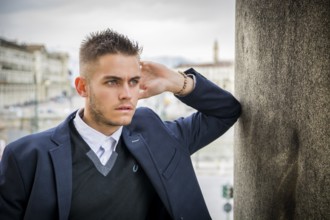Handsome young man outdoor wearing jacket and shirt standing by historic building in European city.