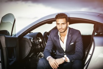Portrait of young attractiave man in business suit sitting in his new stylish car outdoor in