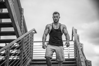 Handsome muscular man standing in city setting looking away to a side, walking down metal stairs