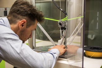 Brunet adult man working with 3D printer, observing the machine at work