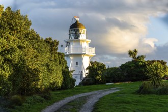 Snow-white picturesque lighthouse at sunset on the Pacific Ocean. South Island, New Zealand.