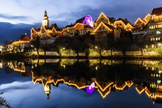 Christmas illuminated house facade of Frohnleiten reflected in the river Mur, blue hour,