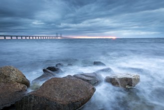 A stormy sea with rocks in the foreground and a bridge in the background, Öresund Bridge,
