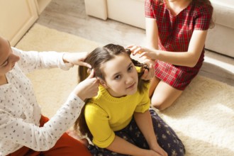 Three girls doing hair sitting on the floor in the room