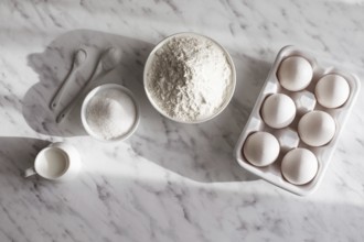 Top view ceramic tray with eggs placed near bowl of flour and sugar. White utensils with white
