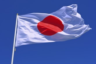 The flag of Japan flutters in the wind in a blue sky with white clouds
