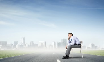 Young businessman sits on an office chair, thoughtful and looking up
