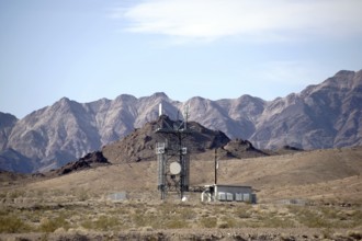A transmitter station stands in the desert in front of the slopes of a mountain range