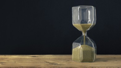 An image of a hourglass on a wooden underground with black background