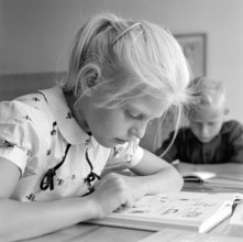 School in the 1950s. A girl is seen sitting at her desk in the classroom reading from the